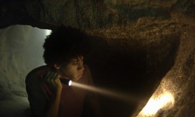 Feijão (Cauê Campos) encontra desenhos e artefatos em gruta misteriosa em "O Sétimo Guardião"